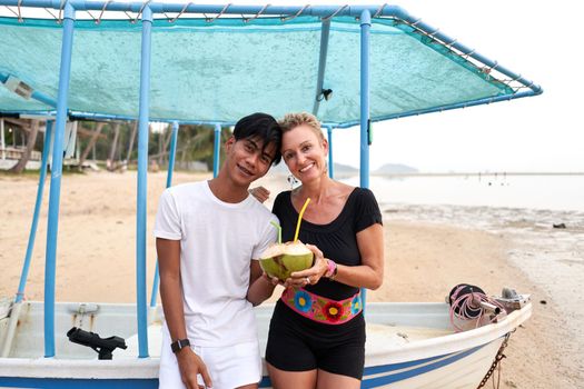 Multicultural couple looking at camera while drinking juice of coconut on a tropical beach