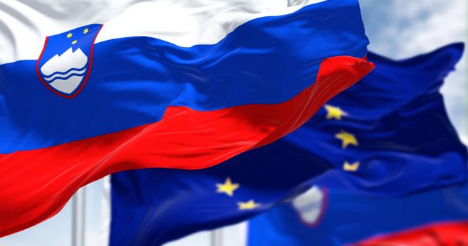 Detail of the national flag of Slovenia waving in the wind with blurred european union flag in the background on a clear day. Democracy and politics. European country. Selective focus.