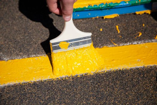 Painting objects in the park in yellow. Yellow oil paint. Work of the park improvement worker. Brush with yellow paint on a pile. Drawing a thick layer of paint on the surface.