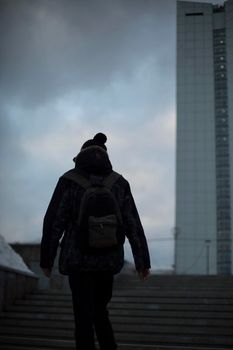 Guy in background of tower. Man in cloudy weather in city. Man walks up stairs.