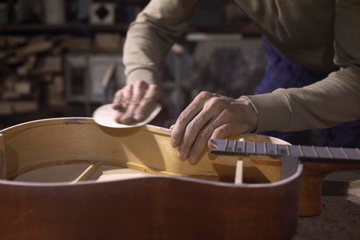 Carpenter repairs guitar. Acoustic guitar without body cover. Guy works in workshop. Creating musical instrument from wood.