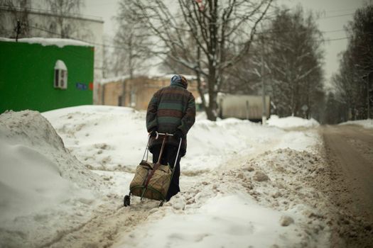 Grandma walks in snow. Woman carries bag on way. Pensioner in city. Woman in winter.
