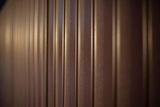 Texture of steel fence. Profile sheet is brown. Fence details. Blurry background in sunlight.