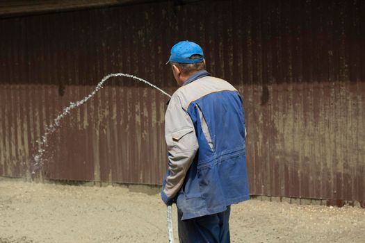 A man washes the fence with a hose. The builder cleans the fence from dirt. Cleaning at a construction site.