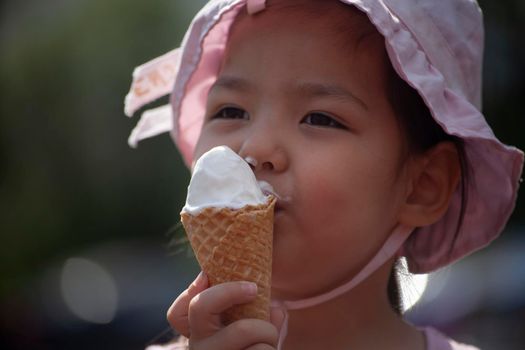 The child is eating ice cream. Girl licking ice cream on the street. A waffle cone in the hands of an Asian child. Portrait of a cute girl with sweetness.