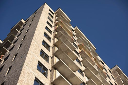 Facade of building. Unfinished house. Windows in new multi-storey building. Plastic windows on street. Balconies without fencing.