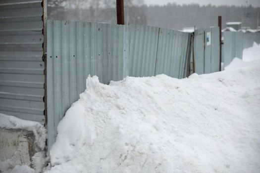 Fence is littered with snow. Fencing around construction site. Metal profile. Details of industrial area after snowfall.