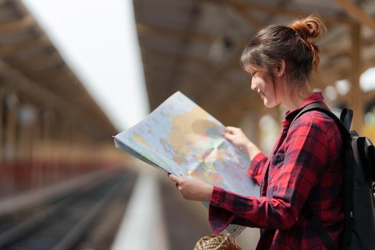 Young traveler woman looking on maps planning trip at train station. Summer and travel lifestyle concept
