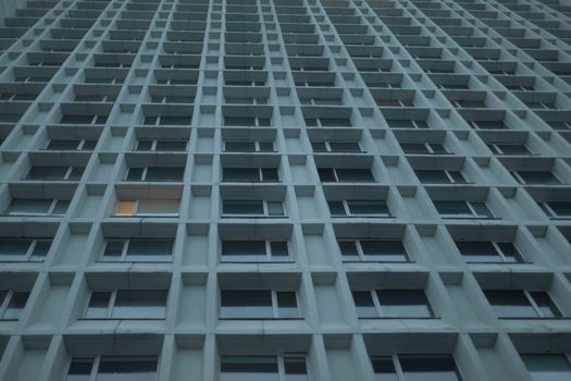 Windows in building are textured. High-rise building in city. Shot from bottom up. Urban architecture. Gray color of house.