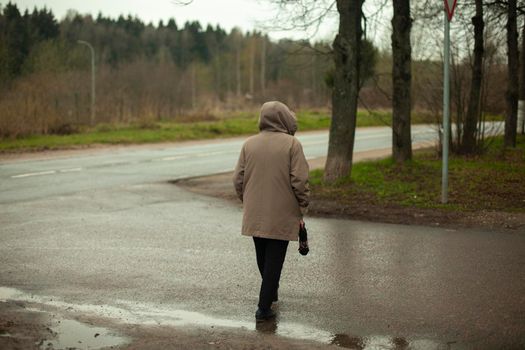 Woman crosses road. Shooting from back. Passerby on street. Cloudy weather. Rainy day.