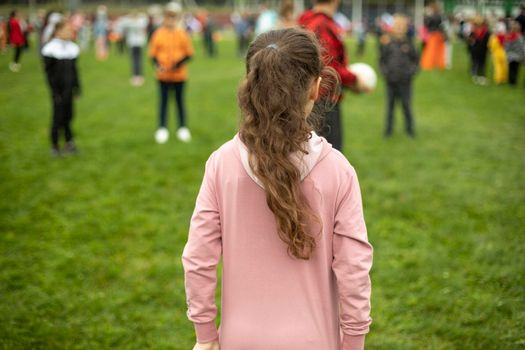 Child does exercises in fresh air. Sports activity for schoolchildren. Children on green grass. Playing in park. Schoolgirl stands with her back.