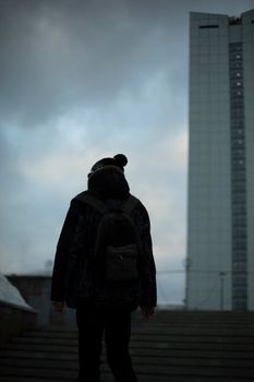 Guy in background of tower. Man in cloudy weather in city. Man walks up stairs.