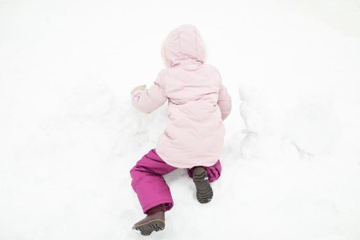 Child plays in snow. Girl in winter. Warm clothes on child. Winter walk in yard.