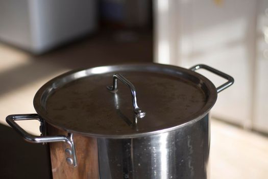 Large pot is heated on stove. Cutlery in kitchen. Details of cooking in dining room. Chrome pan in sunlight.