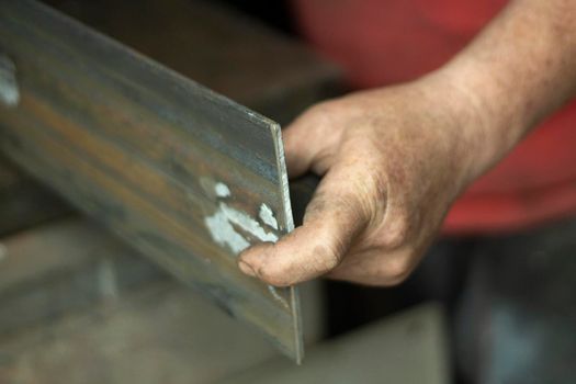 Worker with metal. The guy holds a steel part. Hard work in a metalworking workshop. Creation of steel construction. The working hands of a man.