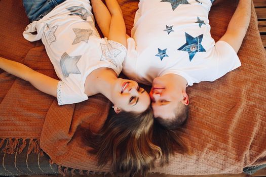 Above view of young couple laying together in bed at studio. Two people smiling and holding hand, spending time together and having fun, wearing in white t-shirt. Concept of love and relationship.
