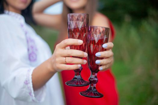 Two girls joined glasses. Wine in glass glass in hands of women. Picnic in nature. Details of holiday in summer.