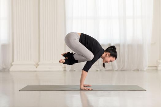 Beautiful young asian woman working out indoors, doing yoga exercise on gray mat, handstand asana, exercise for arms and wrists strength, Crane Crow Pose, Bakasana.