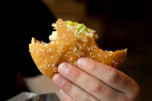 Sandwich in hand. Bun with sesame. Fat lunch. Food in the restaurant. Delicious fast food.