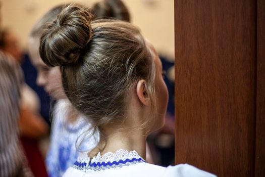 Hairstyle hair tied in a bun. The girl is looking out the door. A teenager with a classic haircut. Human head rear view.