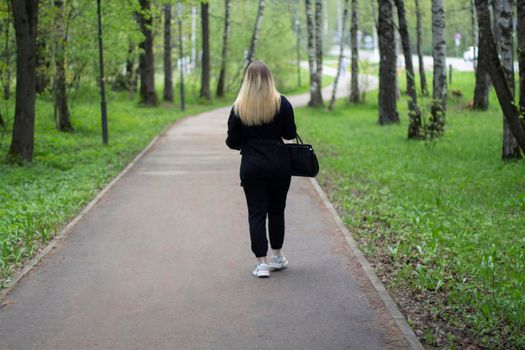 The girl is walking in the park. A woman from the back in the street. A woman walks down the street alone.