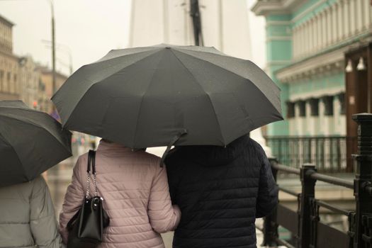 Family with black umbrellas. People rain. Parents with their daughter walk around the city. Bad weather on the street.