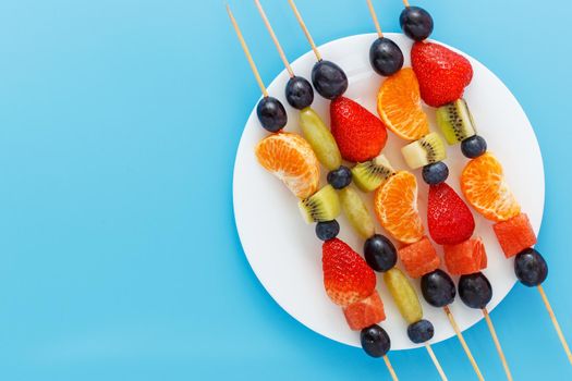 Fresh fruit skewers on a plate for a healthy snack on a blue background. copy space