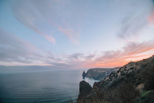 A red burning sunset with the silhouette of a cliff over the sea. Abstract nature summer or spring ocean sea background. Small waves on golden warm water surface with bokeh lights from sun.