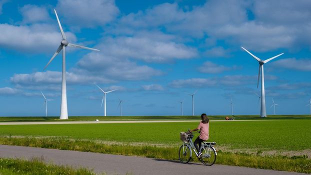 young woman electric green bike bicycle by windmill farm, windmills isolated on a beautiful bright day Netherlands Flevoland Noordoostpolder