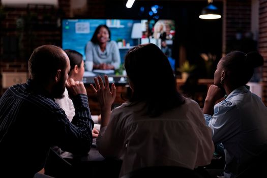 Woman waving hello in online video conference with african american entrepreneur and colleagues working remote from home. Coworkers greeting company clients in internet call in late night meeting.