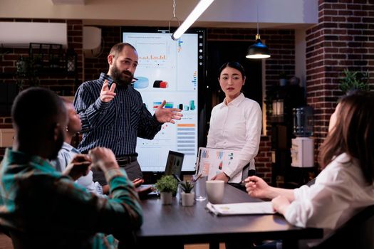 Diverse multiethnic business people analyzing management strategy working overtime in company office meeting room late at night. Sales team discussing marketing strategy in startup workspace.