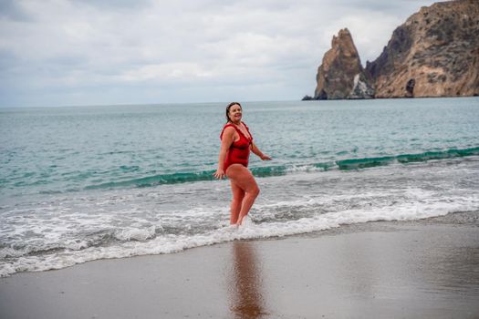 Woman in a bathing suit at the sea. A fat young woman in a red swimsuit enters the water during the surf.