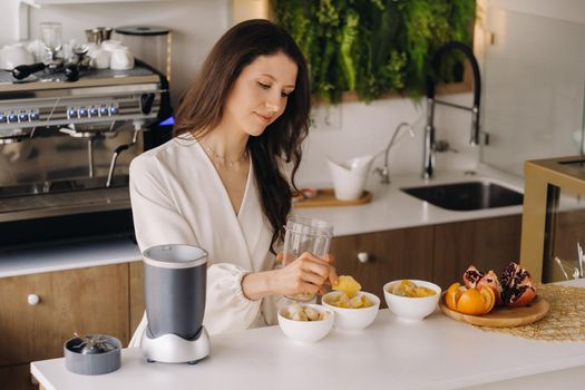 a girl makes a detox cocktail of fruit in the kitchen . Diet for weight loss.