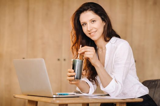 A young freelance woman with a cocktail in her hands at her workplace at work.