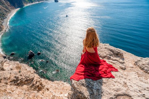 A girl with flowing hair in a long red dress sits on a rock above the sea. The stone can be seen in the sea