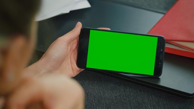 Woman sitting on a sofa with smart phone in horizontal mode . Phone with Greenscreen and Chroma Key. Mock Up with Tracking Markers and Alpha Matte. Caucasian Female Looking at Isolated Colour of Cellp