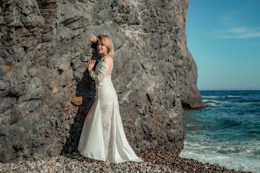 Middle aged woman looks good with blond hair, boho style in white long dress on the beach decorations on her neck and arms