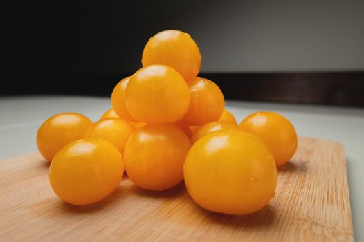 Close-up shot of yellow cherry tomatoes on a wooden cutting board in the kitchen on a white table.