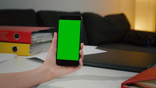 Woman at home relaxing reading on the smartphone with pre-keyed green screen, Chromakey Mockup. Talks on the phone, gesturing with hands. Business woman from home office has important phone video call