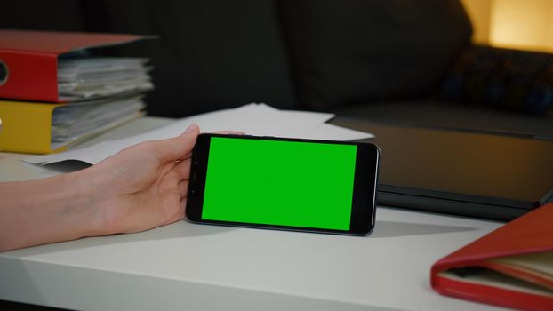 Woman looking at smartphone phone with green screen chroma key display sitting at office desk. Business woman using a Smart phone. Hand of man holding mobile smart phone with chroma key, new technolog