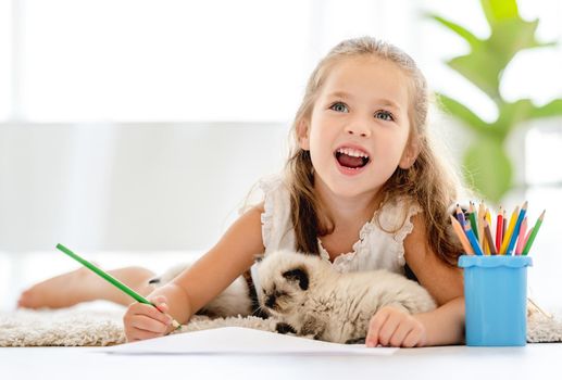 Child girl painting with ragdoll kittens on the floor and imagining. Little female person drawing with colorful pencils and kitty pets close to her at home