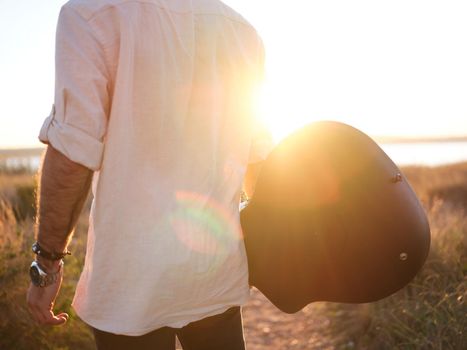 man posing backwards holding his guitar and watching the sunset in the background, horizontal