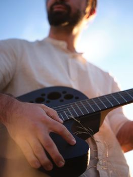 upward focus on a man holding a guitar and covering the sun, blurred background