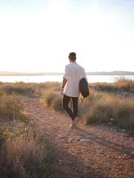 man walking with his guitar in the countryside going to the lake to watch the sunset