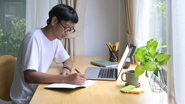 Side view young male freelancer using laptop, working online at home.