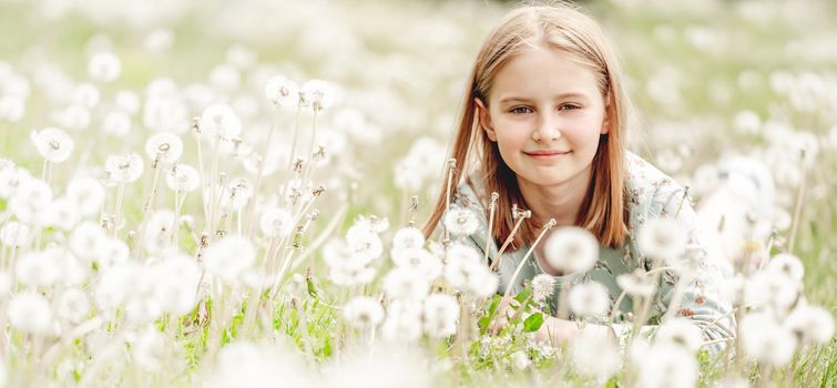 Little girl sitting in blowballs flowers field and smiling. Cute child kid with dandelions at nature