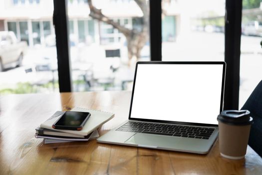 Laptop computer, coffee cup and notebook on wooden office desk.