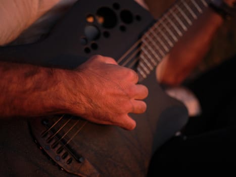 close-up view of a man playing the guitar in the sunlight, horizontal picture, blurred background