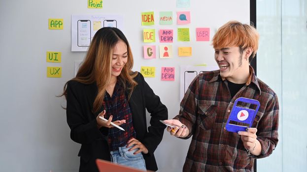 Two happy web designers presenting and testing mobile app interface design on whiteboard at creative office.