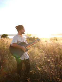 man standing with a guitar in the middle of a field with the sunset on the horizon